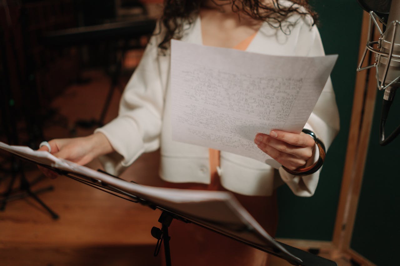A female musician holds and reads lyrics on paper in a professional recording studio.