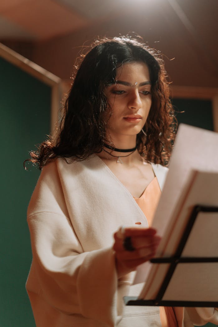 Confident woman in recording studio reading a music sheet, focused on her performance.
